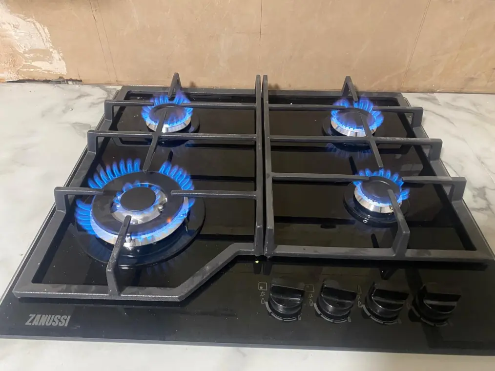 A four-burner gas hob set into a worktop, all four rings lit with a blue flame.