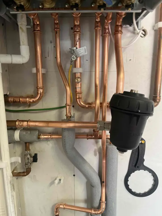 A copper manifold and pressure-reducing valve behind a wall-mounted combi boiler, with lagged pipe runs.