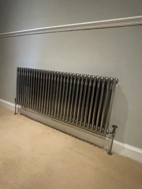 A gunmetal multi-column radiator fitted against a warm beige wall.
