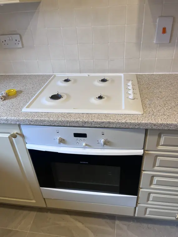 A gas hob set into a worktop over a built-under electric oven, with a tiled splashback.